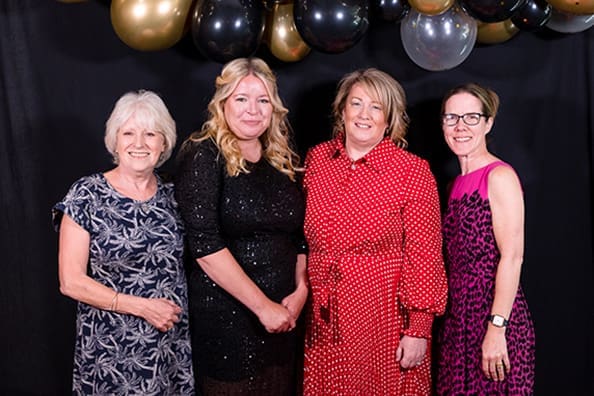 Four women pose together in front of a black and gold balloon arch at the Golden Age Gala 2025 at the Parkgate Hotel Cardiff