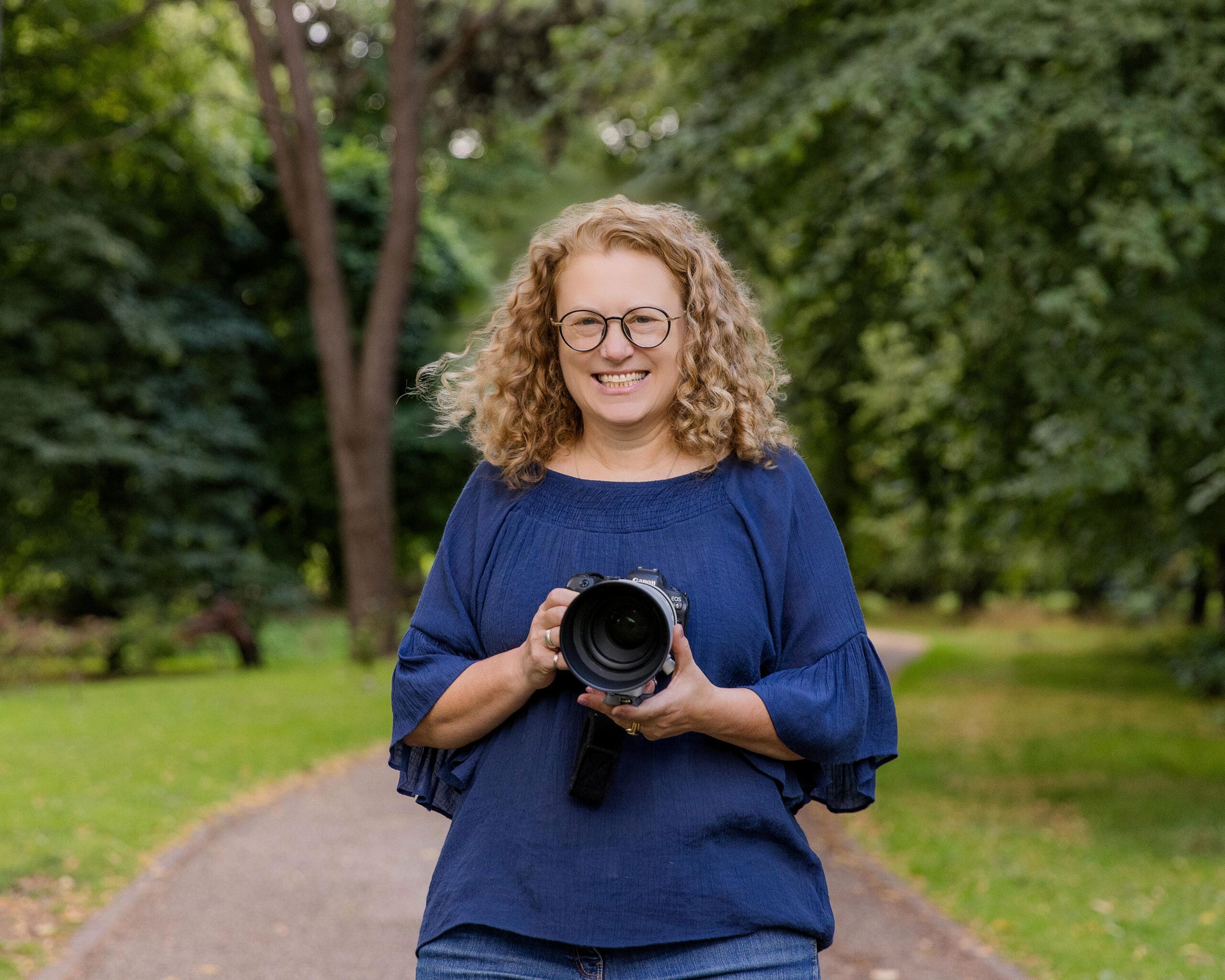 2025-07-29 Jo Branding Images -1033 Jo Davies of Jo Davies Photography holding a camera on a pathway amongst some trees
